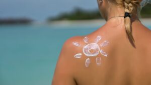 Schiena abbronzata di una donna bionda che è rivolta verso il mare: sulla spalla sinistra c'è un sole disegnato con la crema solare