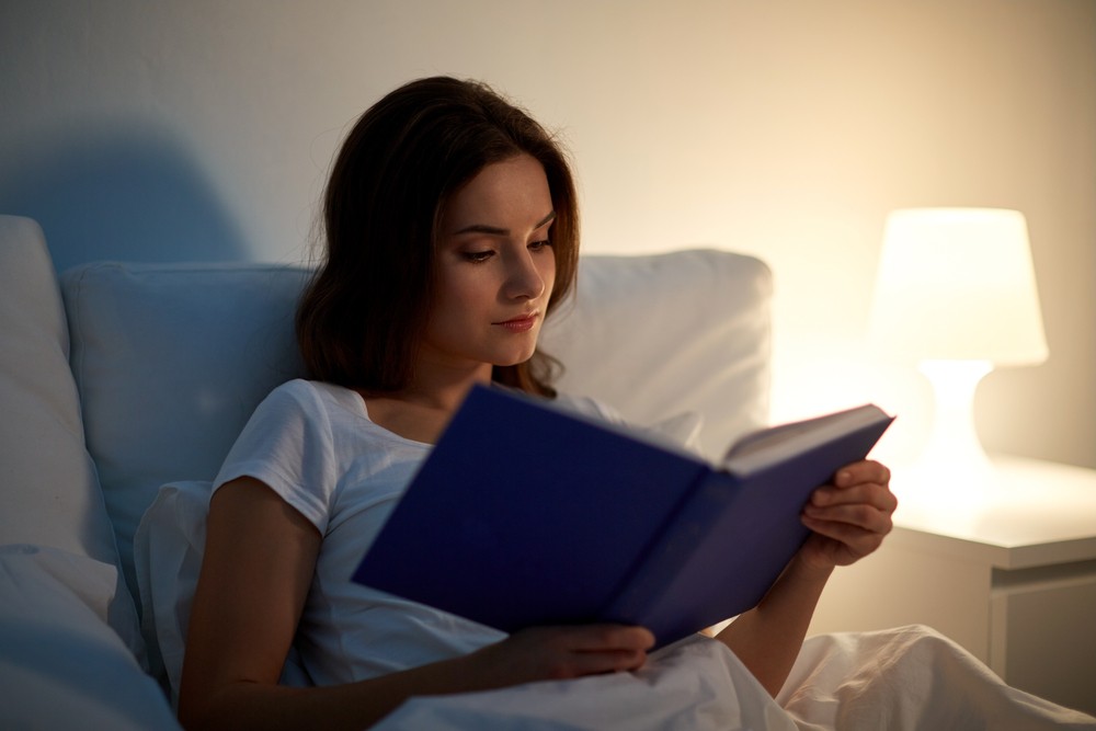Donna legge un libro sul letto per contrastare l'insonnia da caldo